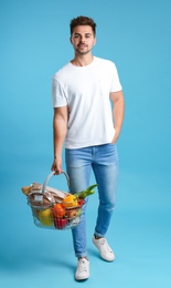 Young man with shopping basket full of products on blue background