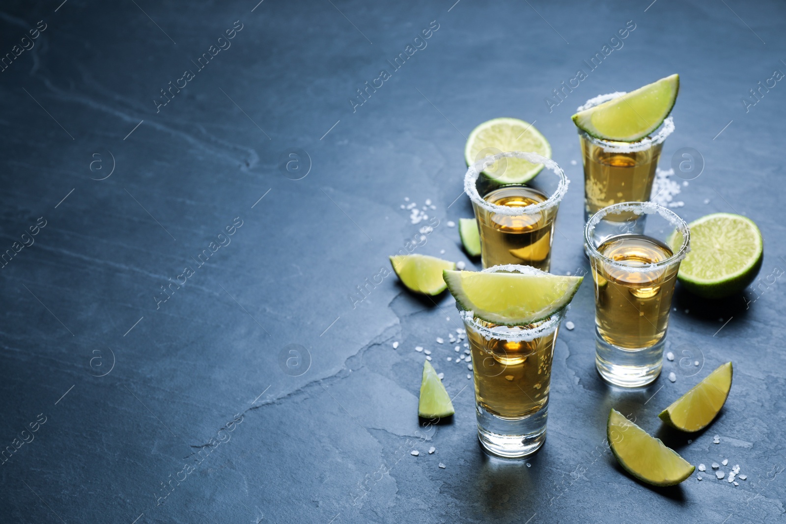 Photo of Mexican Tequila shots with salt and lime slices on grey table. Space for text