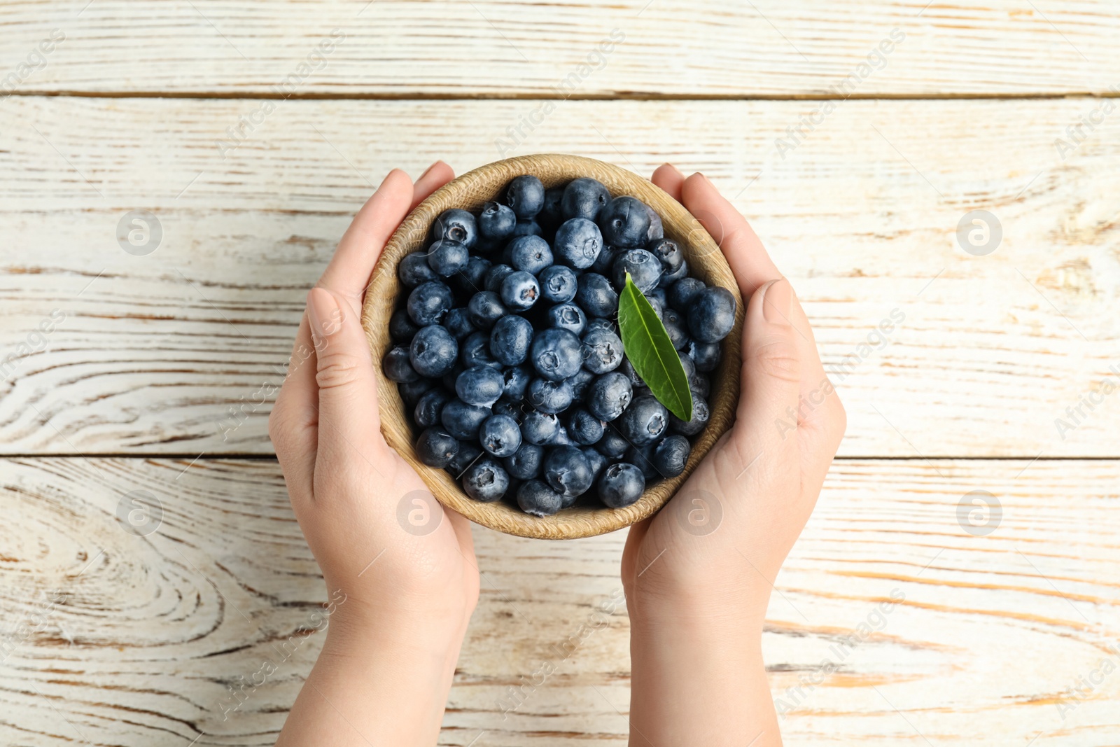 Photo of Woman holding juicy fresh blueberries at white wooden table, top view