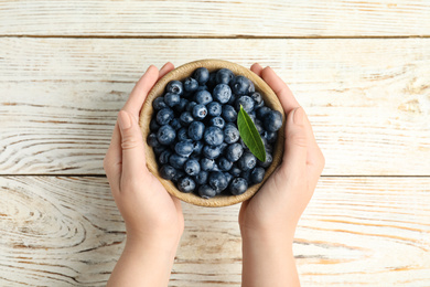 Photo of Woman holding juicy fresh blueberries at white wooden table, top view