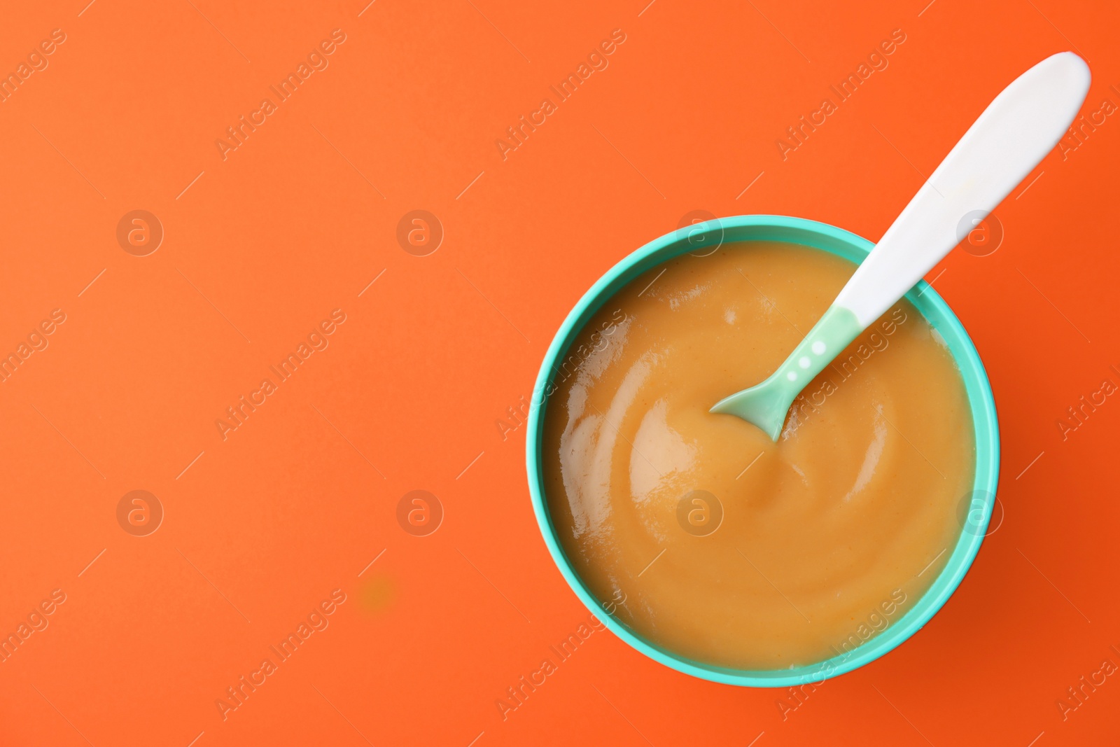 Photo of Bowl of healthy baby food an space for text on color background, top view