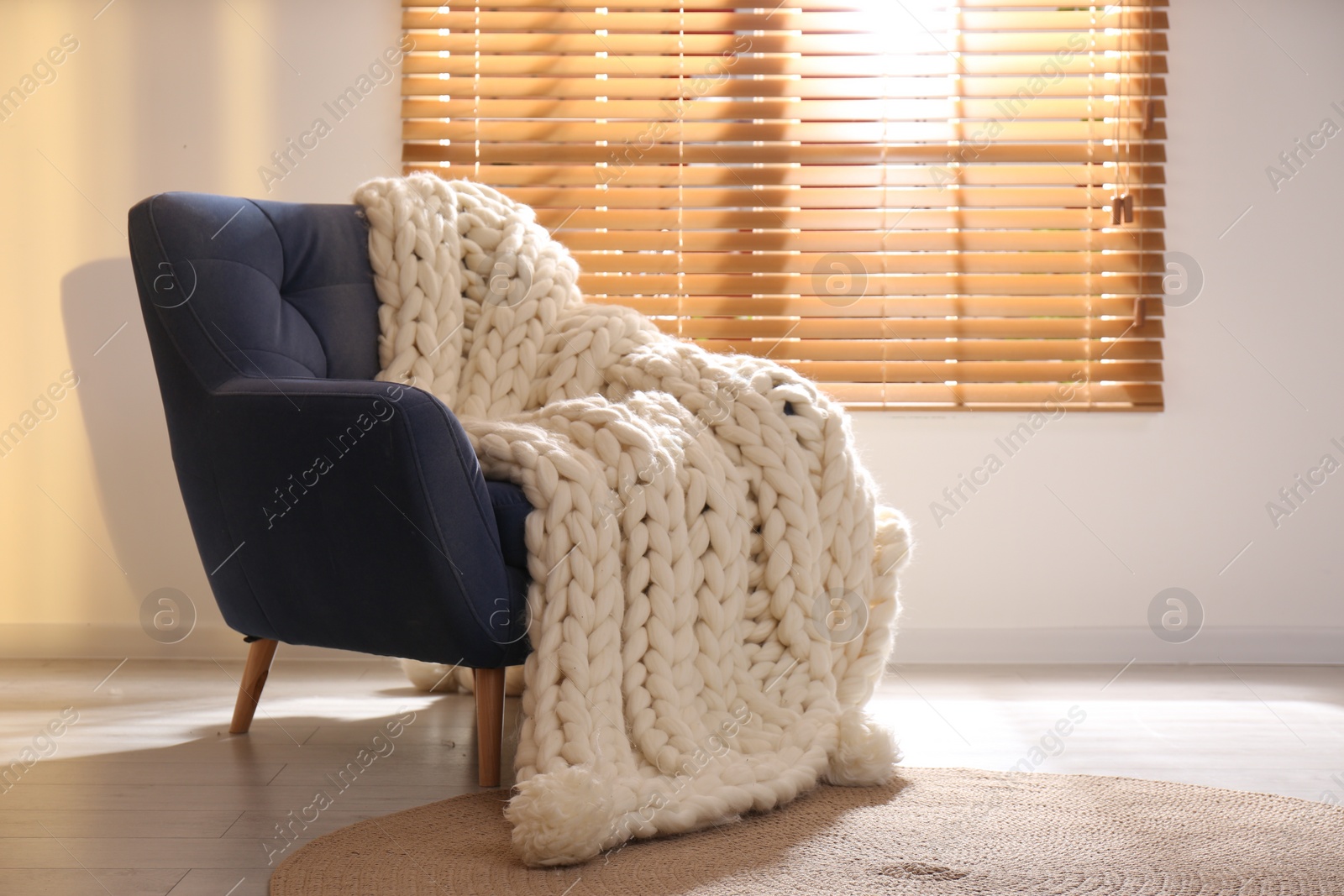 Photo of Soft knitted blanket on armchair in living room. Interior element