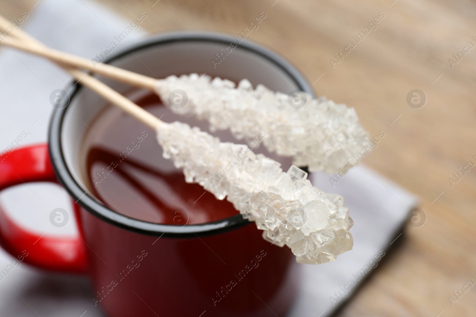 Photo of Sticks with sugar crystals and cup of tea on table, closeup