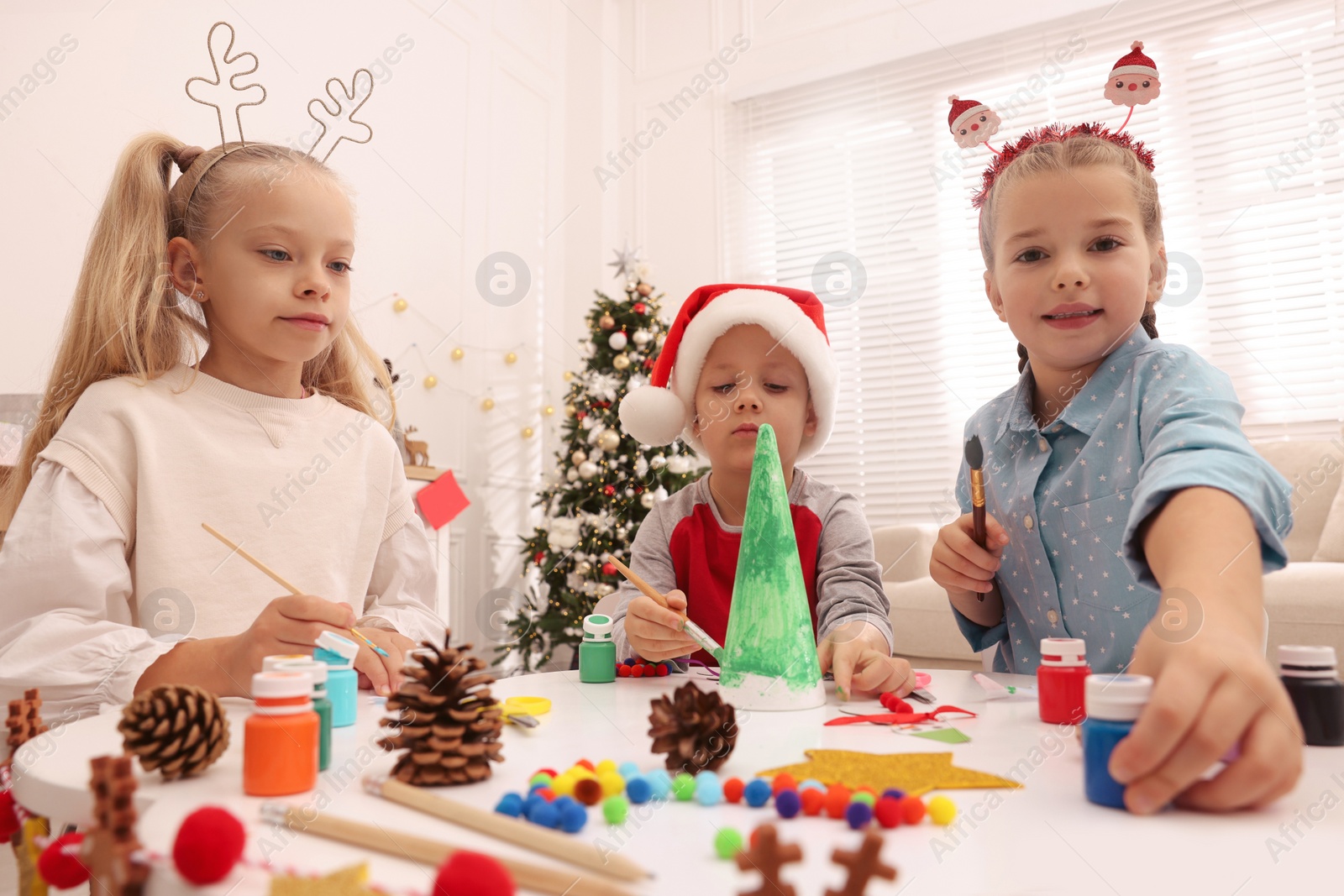 Photo of Cute little children making Christmas crafts at table in decorated room