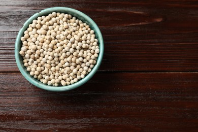 Photo of Aromatic spice. White pepper in bowl on wooden table, top view. Space for text