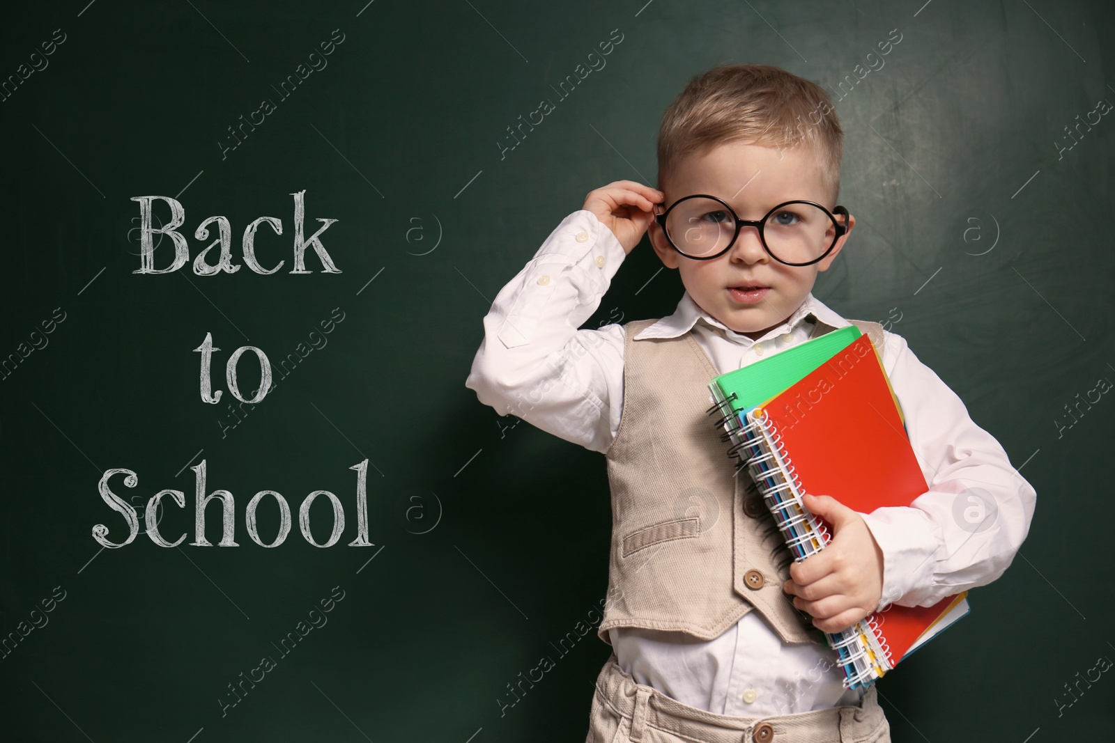 Image of Cute little child wearing glasses near chalkboard with phrase BACK TO SCHOOL