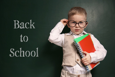 Image of Cute little child wearing glasses near chalkboard with phrase BACK TO SCHOOL