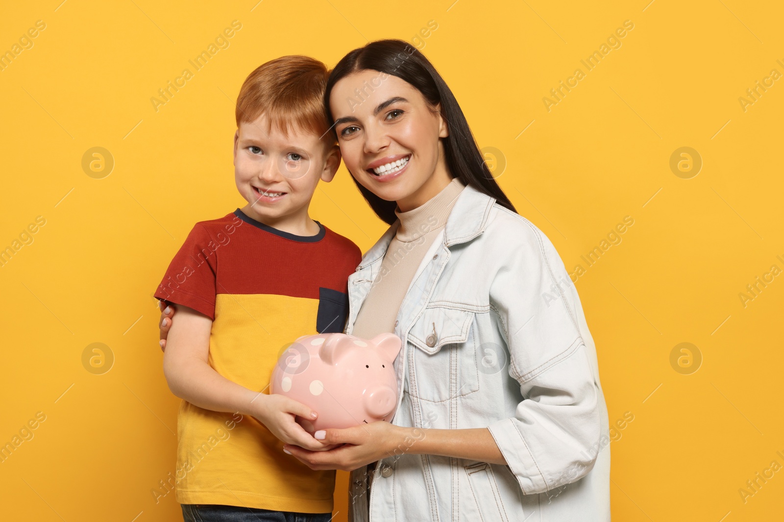 Photo of Mother and her son with ceramic piggy bank on orange background