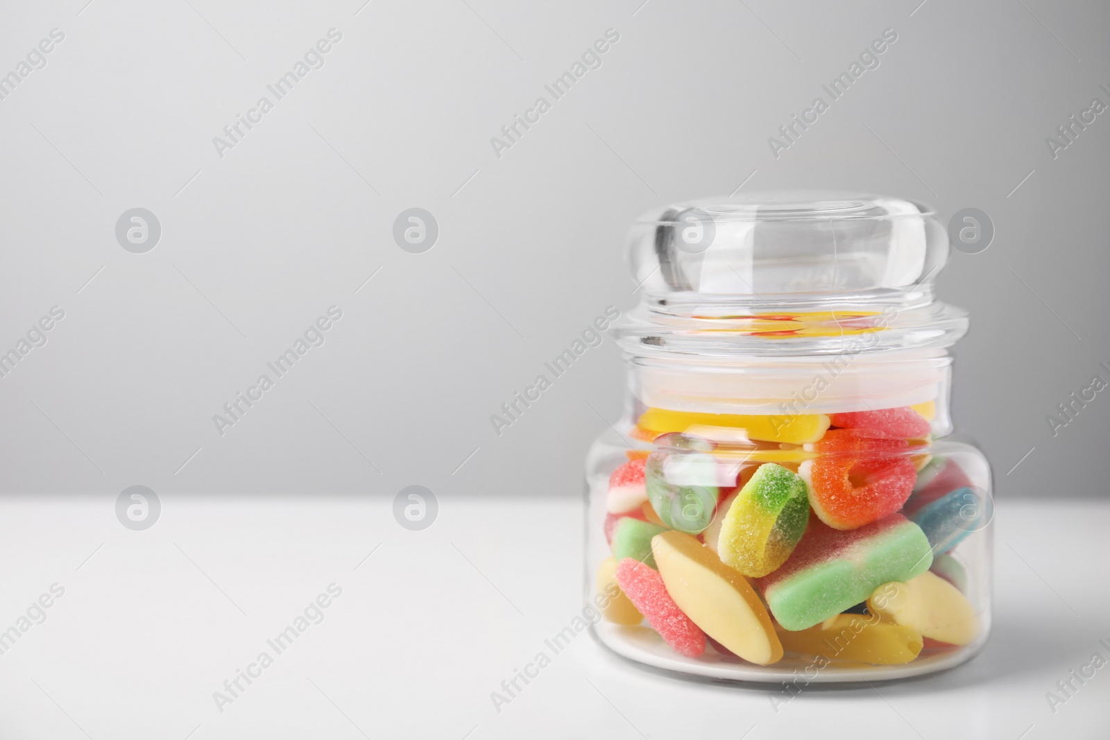 Photo of Tasty jelly candies in jar on white table, space for text