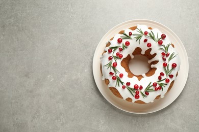 Traditional Christmas cake decorated with glaze, pomegranate seeds, cranberries and rosemary on light grey table, top view. Space for text