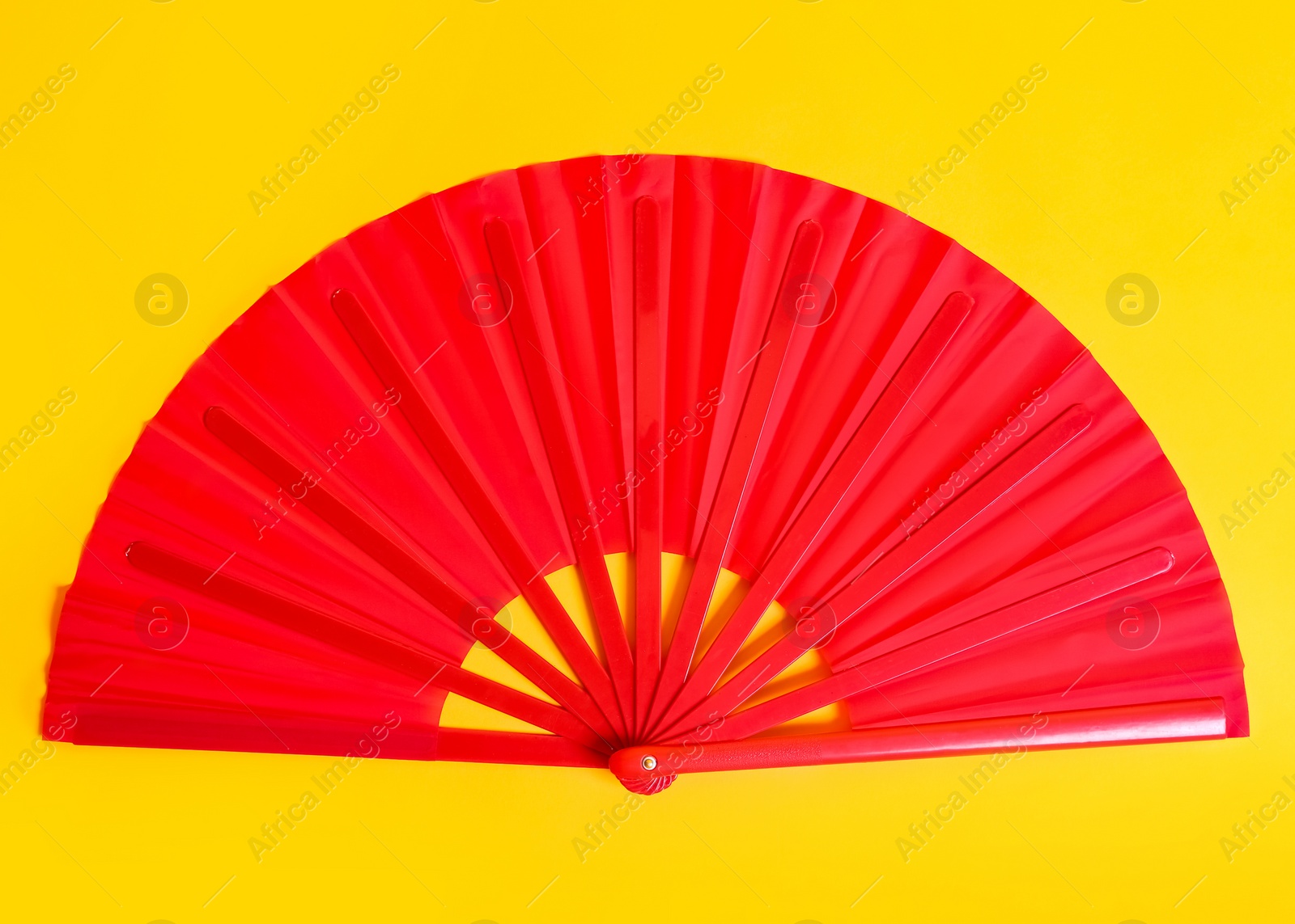 Photo of Red hand fan on yellow background, top view