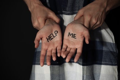 Photo of Man holding woman's hands with words HELP ME on dark background, closeup. Stop sexual assault