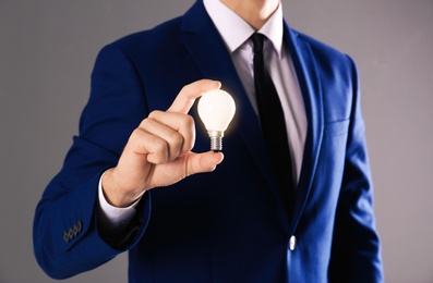Photo of Businessman holding lamp bulb against gray background, closeup
