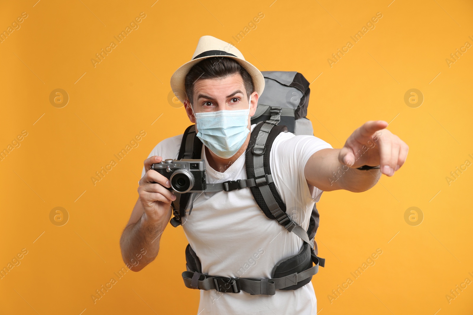 Photo of Male tourist in protective mask with travel backpack and camera on yellow background