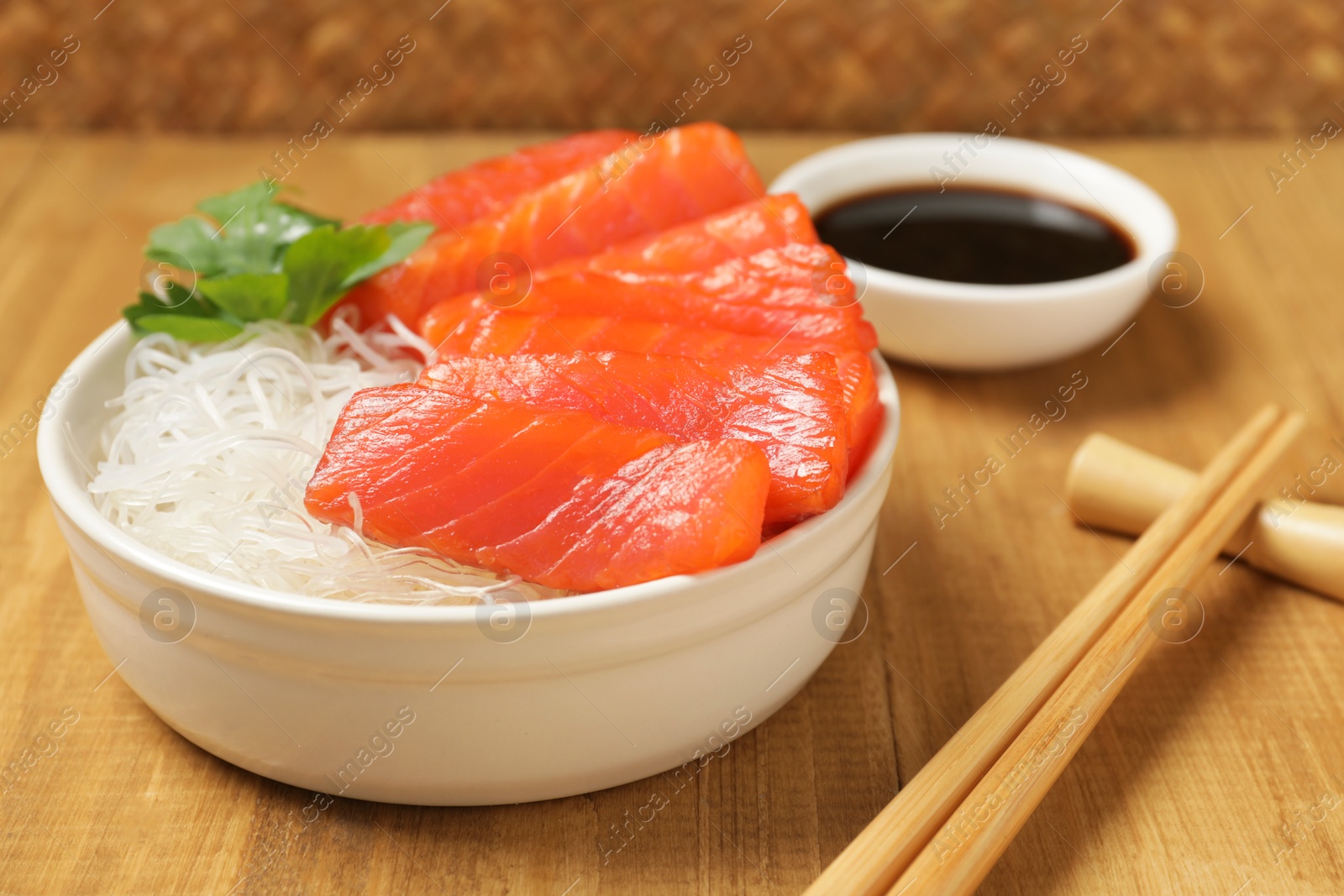 Photo of Delicious salmon sashimi served with funchosa, soy sauce and parsley on wooden table, closeup