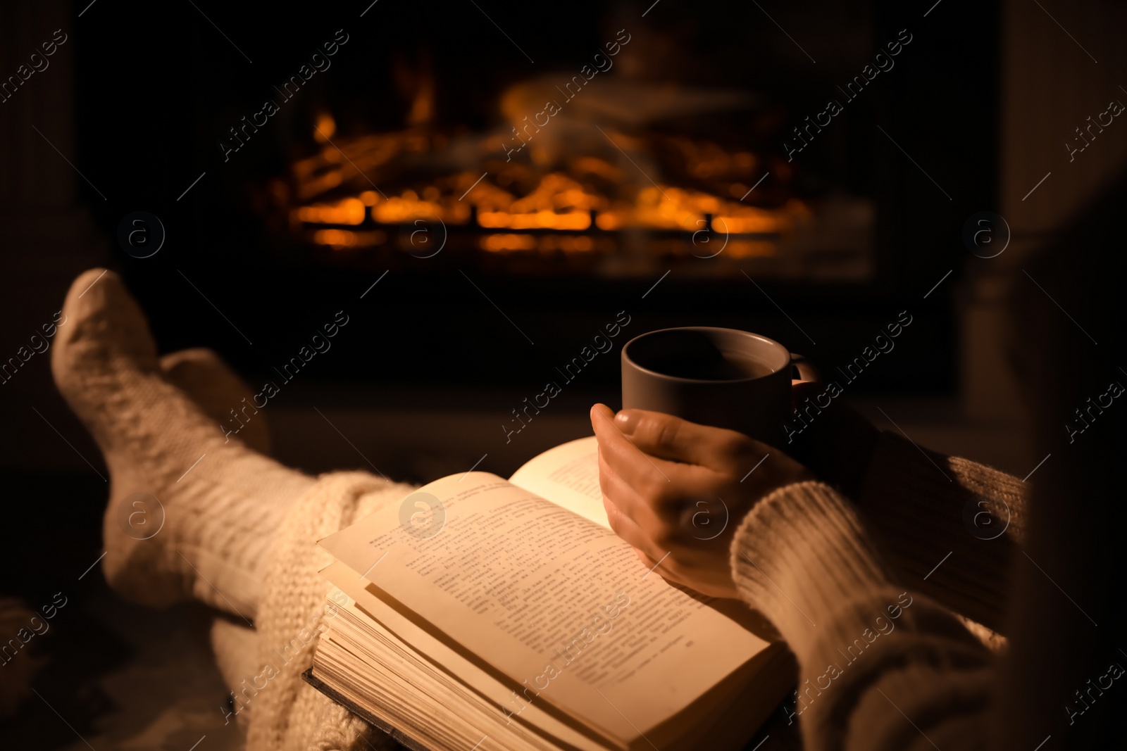 Photo of Woman with book and cup near fireplace indoors, closeup. Cozy atmosphere