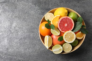 Photo of Different fresh citrus fruits and leaves in bowl on grey textured table, top view. Space for text