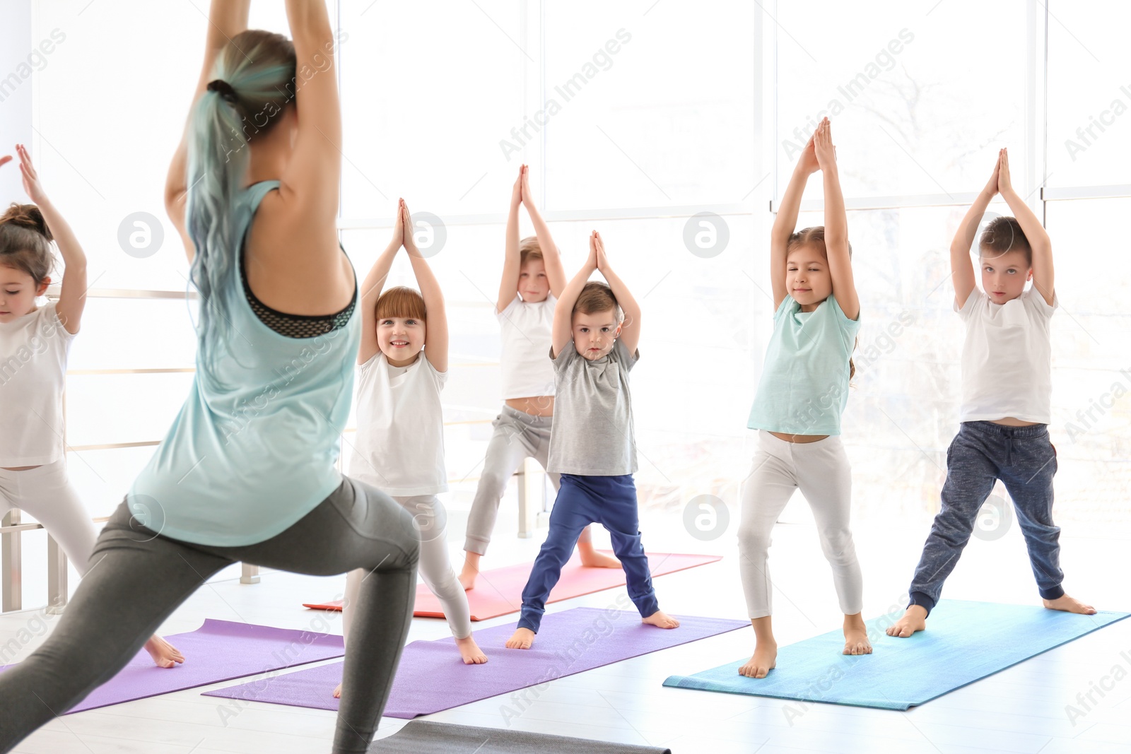 Photo of Little children and their teacher practicing yoga in gym