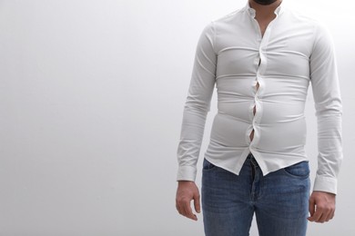 Man wearing tight shirt on white background, closeup. Overweight problem