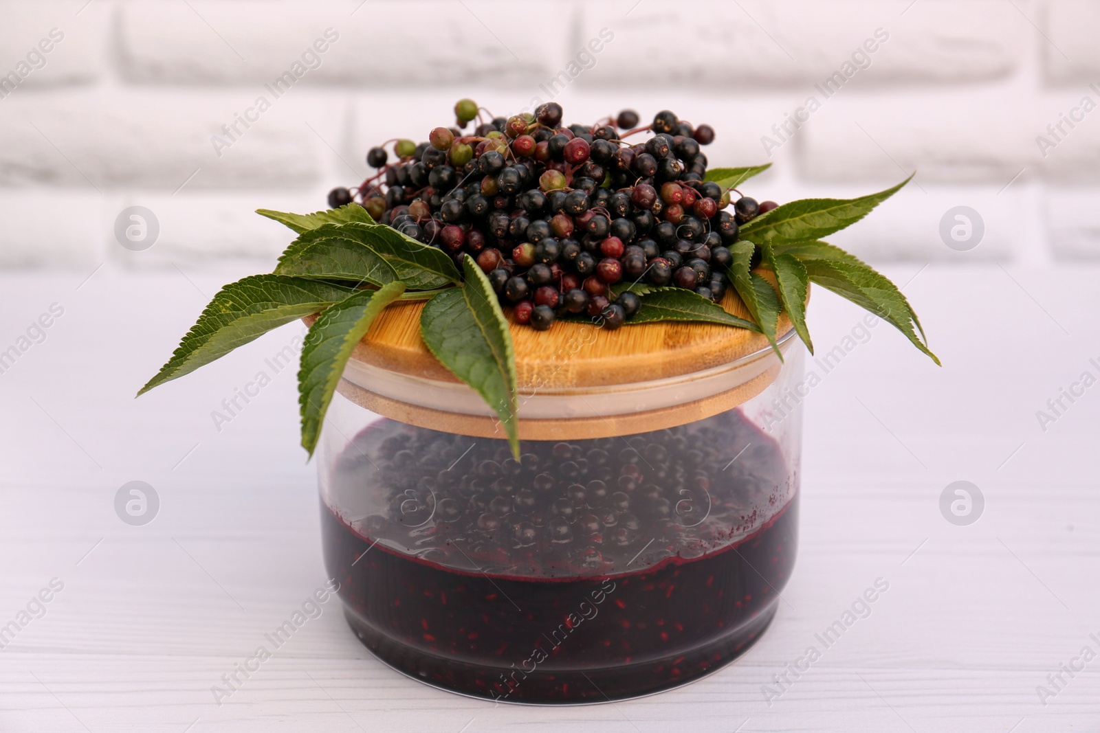 Photo of Glass jar with elderberry jam and Sambucus berries on white wooden table