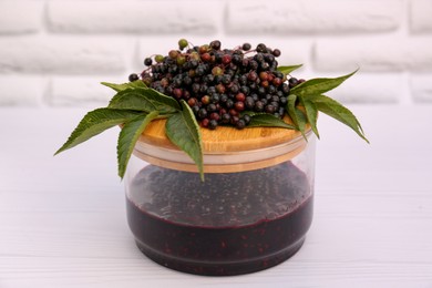 Glass jar with elderberry jam and Sambucus berries on white wooden table