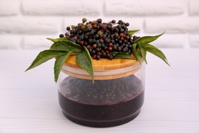 Photo of Glass jar with elderberry jam and Sambucus berries on white wooden table