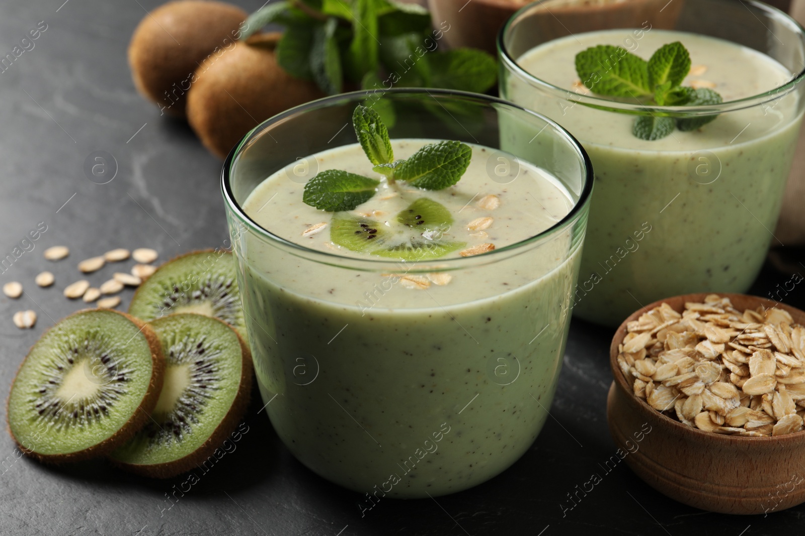 Photo of Glasses of tasty kiwi smoothie with oatmeal on dark table