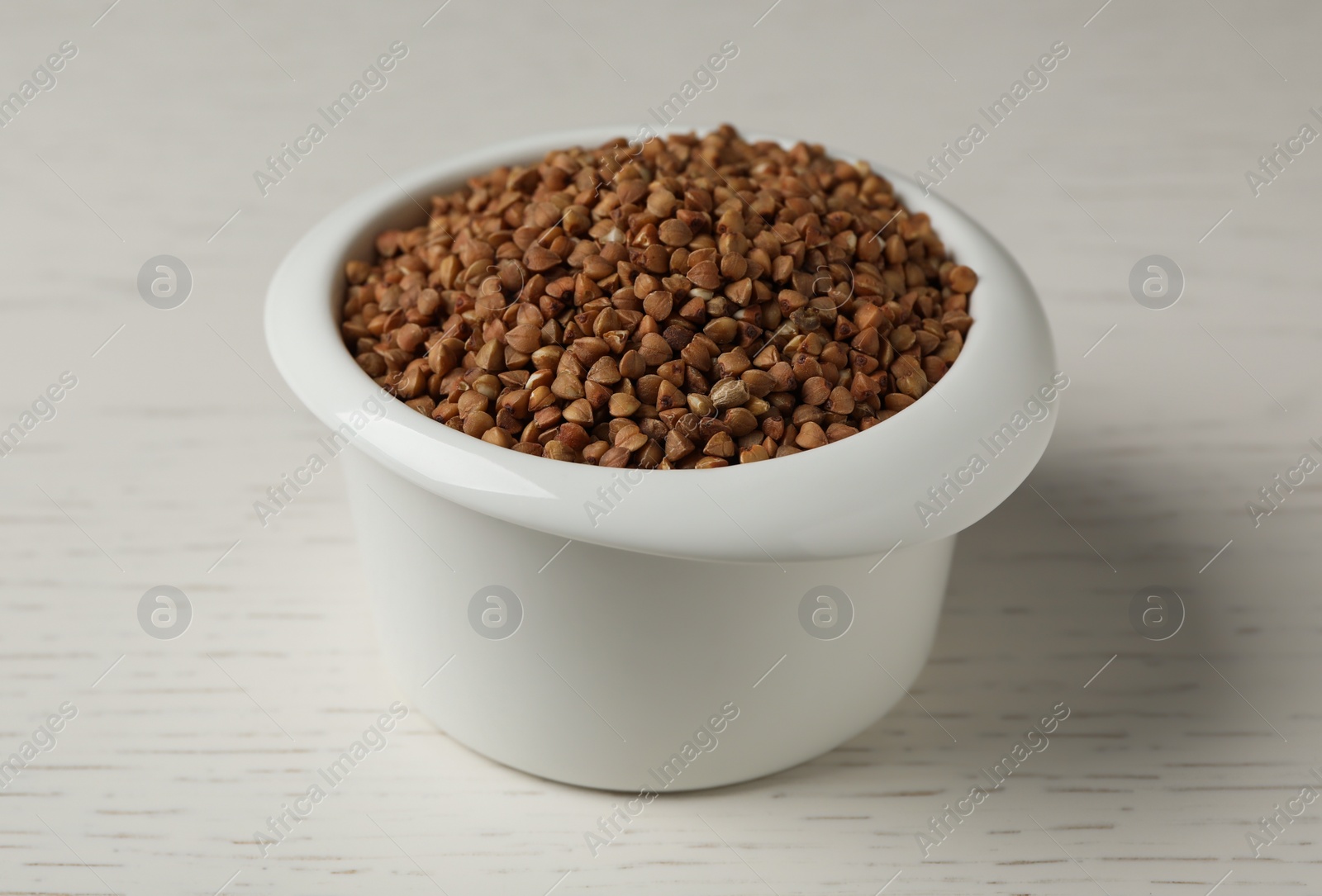 Photo of Uncooked buckwheat in ceramic bowl on table