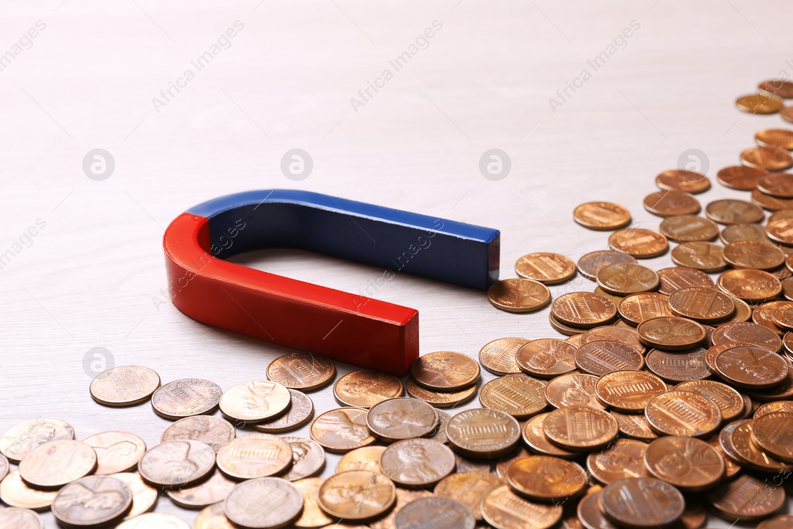 Photo of Red and blue horseshoe magnet attracting coins on light wooden background