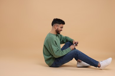 Handsome young man using smartphone on beige background, space for text