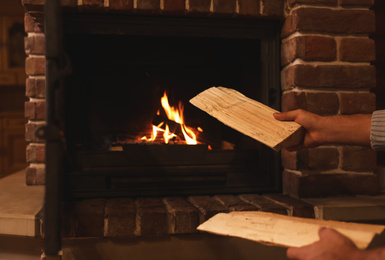 Photo of Man putting dry firewood into fireplace at home, closeup. Winter vacation