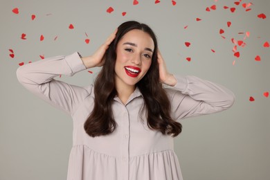 Photo of Beautiful young woman under falling heart shaped confetti on grey background