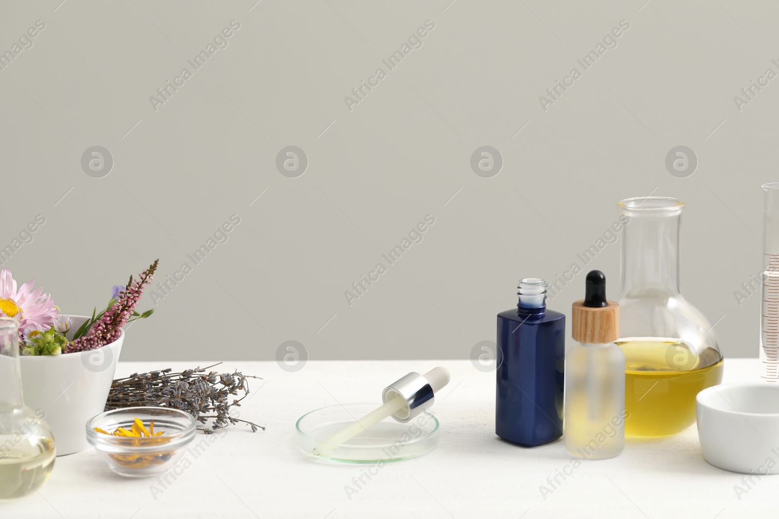 Photo of Developing cosmetic oil. Laboratory glassware and flowers on white table, space for text