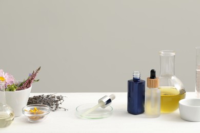 Developing cosmetic oil. Laboratory glassware and flowers on white table, space for text