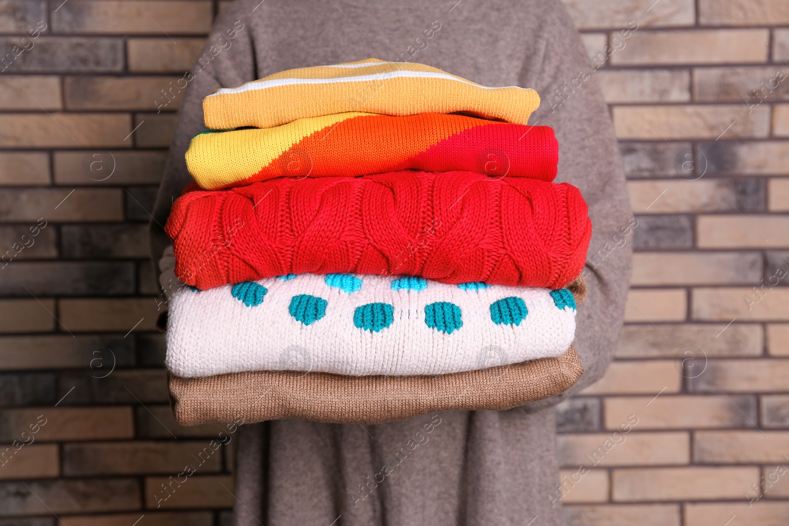 Photo of Woman holding stack of colorful winter clothes near brick wall