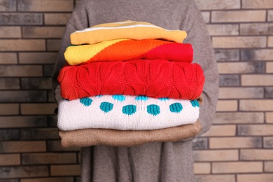 Photo of Woman holding stack of colorful winter clothes near brick wall