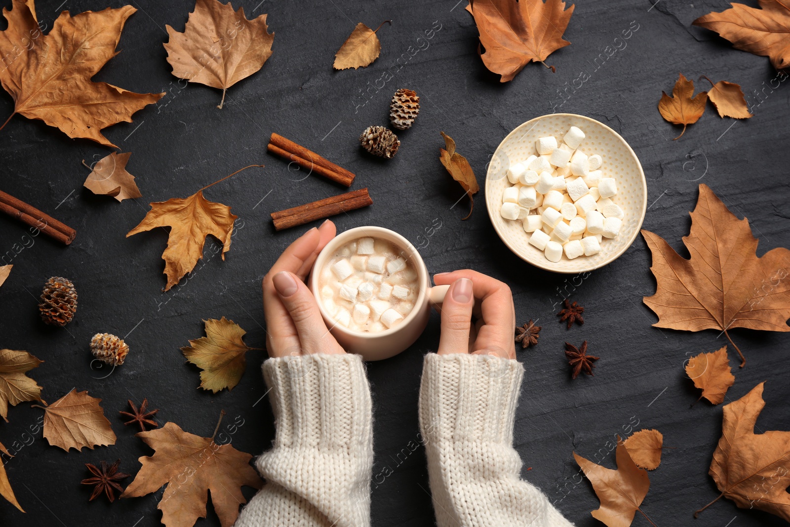 Photo of Woman with cup of hot drink at black table, top view. Cozy autumn atmosphere