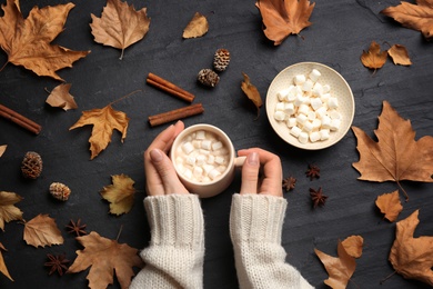 Photo of Woman with cup of hot drink at black table, top view. Cozy autumn atmosphere