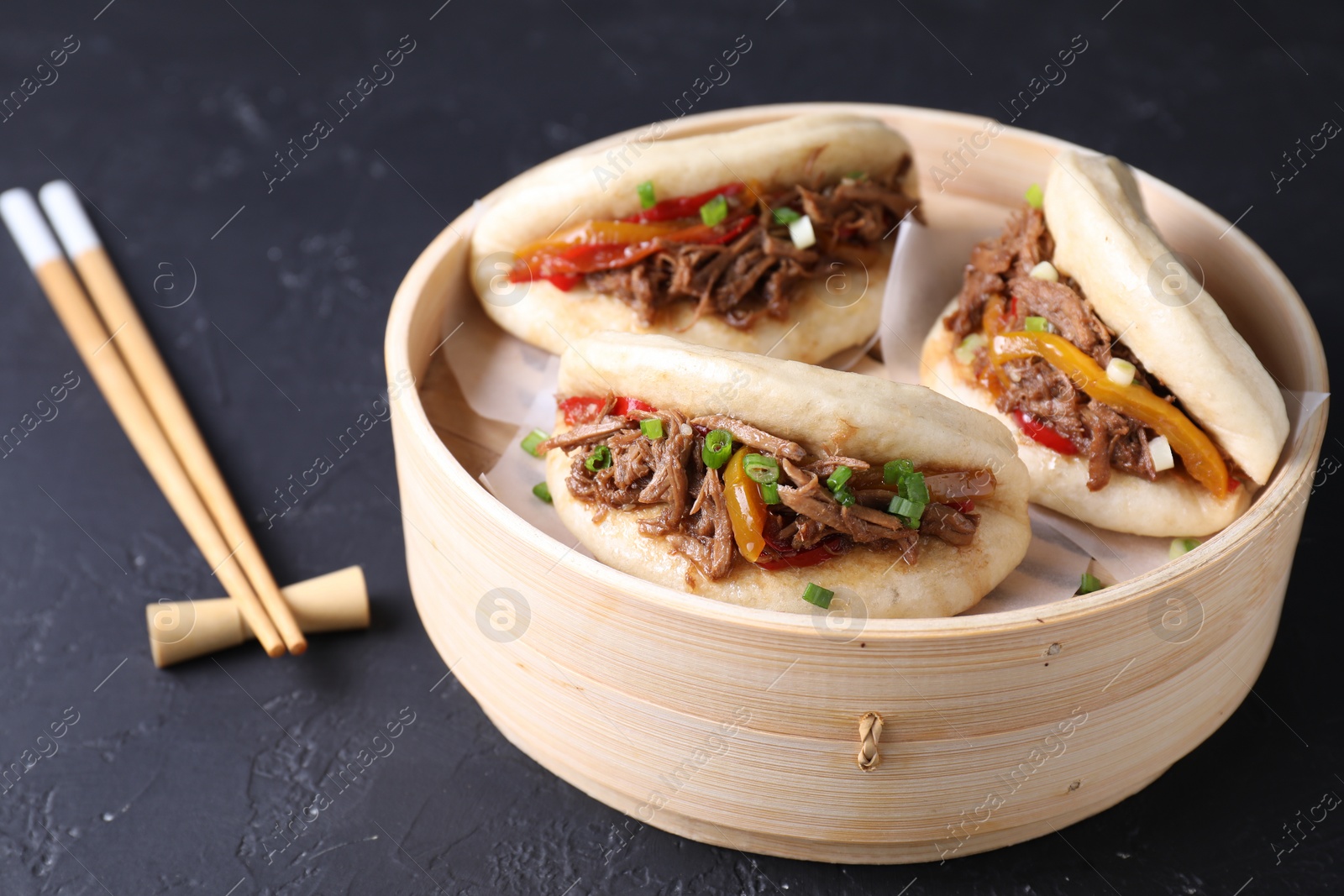 Photo of Delicious gua bao in bamboo steamer and chopsticks on black table