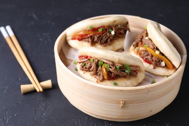 Delicious gua bao in bamboo steamer and chopsticks on black table
