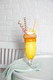 Glass of tasty milk shake with sweets on table near brick wall