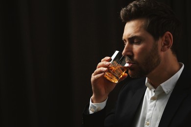 Photo of Man in suit drinking whiskey on black background. Space for text
