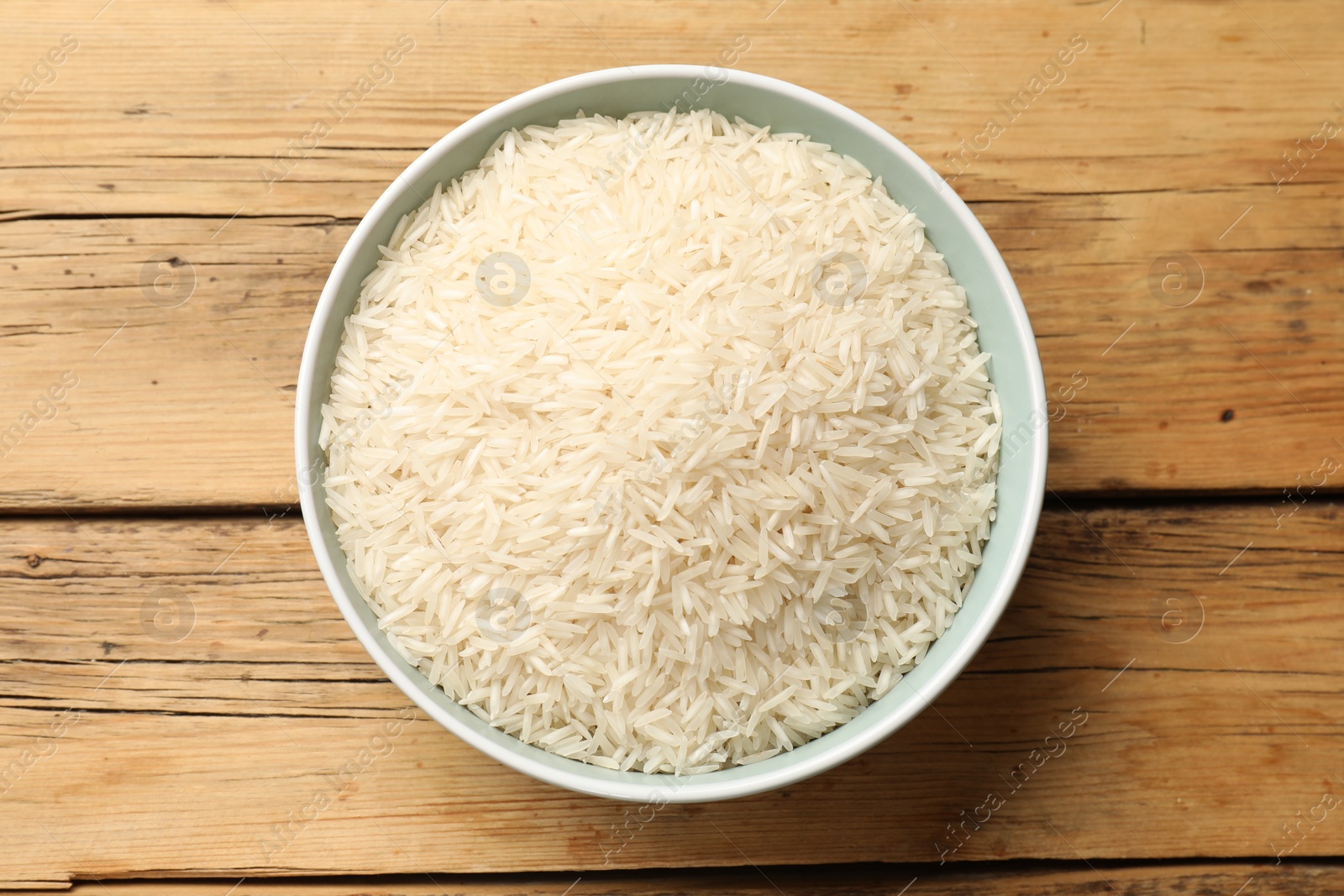 Photo of Raw basmati rice in bowl on wooden table, top view