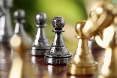 Golden and silver pawns on chess board against blurred background, closeup