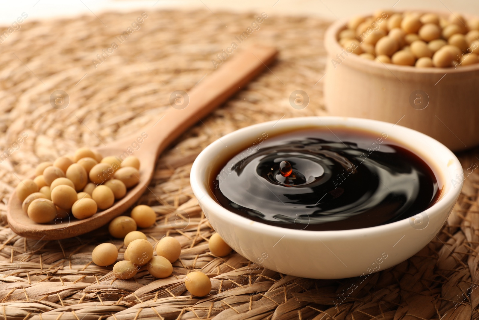 Photo of Soy sauce drop falling into bowl on wicker mat, closeup