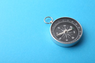 Photo of One compass on light blue background, space for text. Tourist equipment