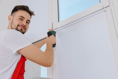 Photo of Worker with drill installing roller window blind indoors