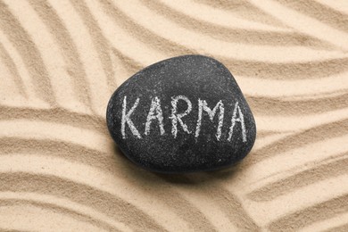Photo of Stone with word Karma on sand, top view