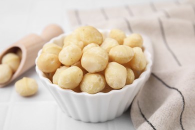 Photo of Tasty peeled Macadamia nuts in bowl on white table, closeup