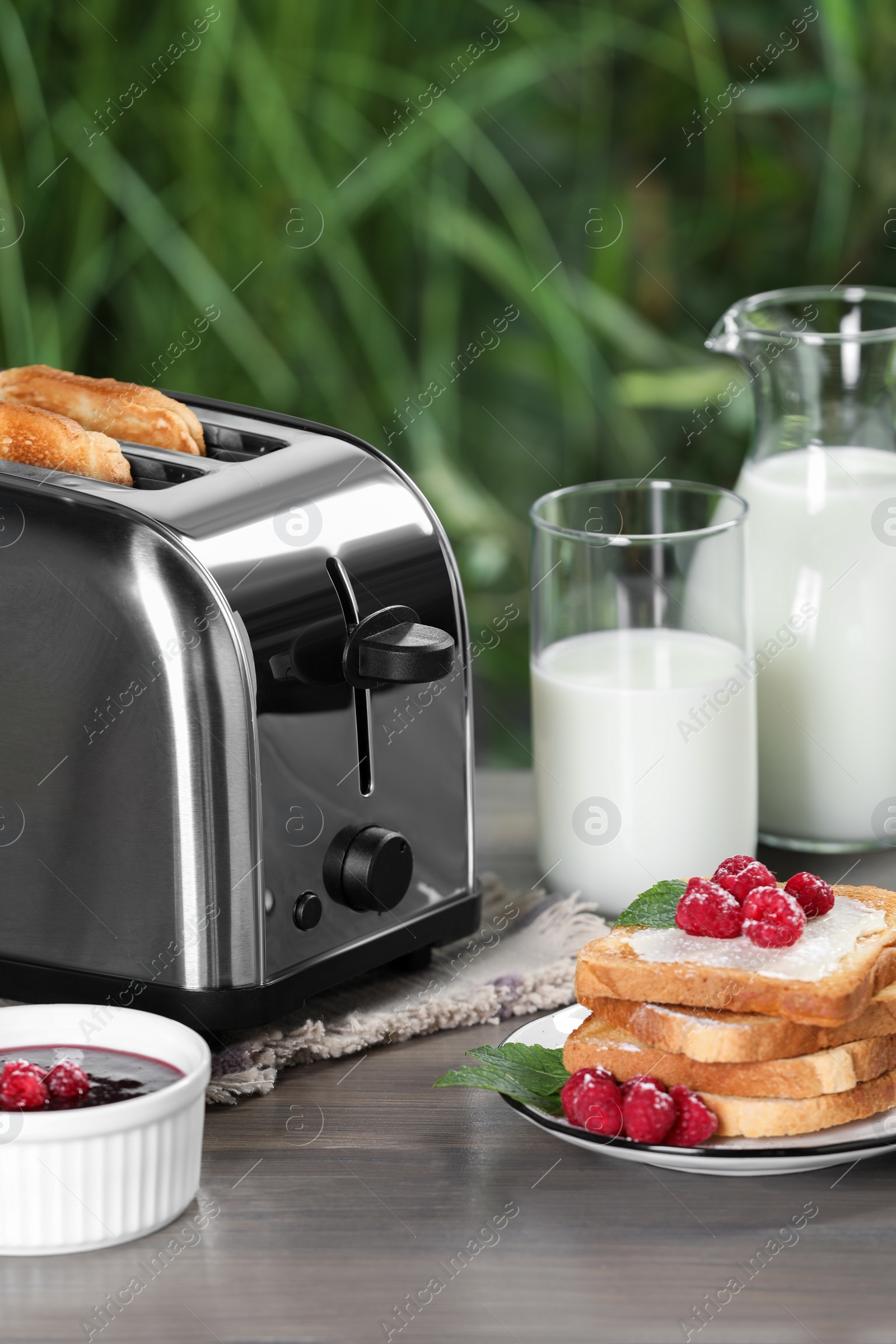 Photo of Toaster with roasted bread, milk and raspberry jam on wooden table. Tasty breakfast